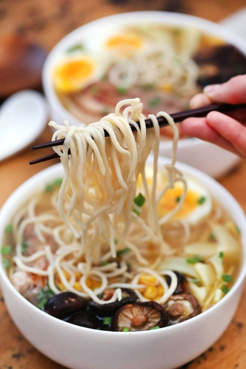 Chopsticks holding ramen noodles above bowl