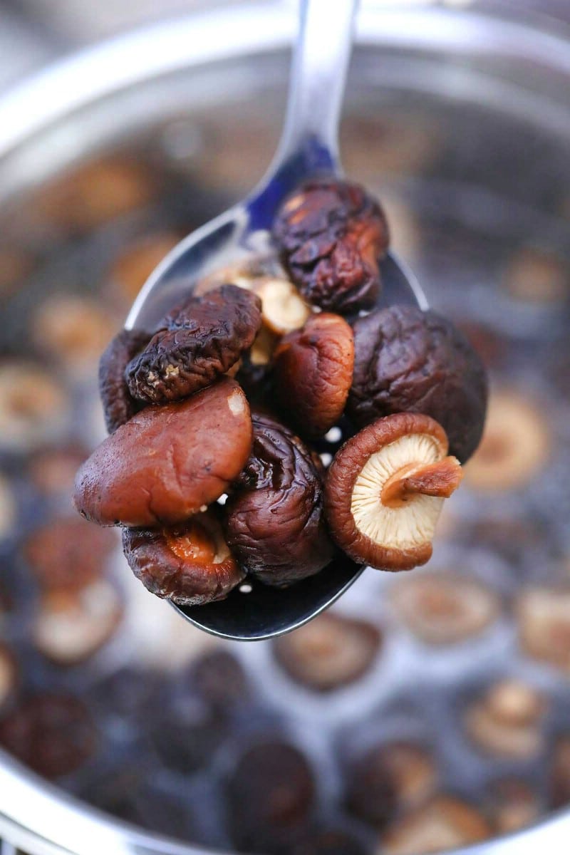 Spoon of shiitake mushrooms over stockpot