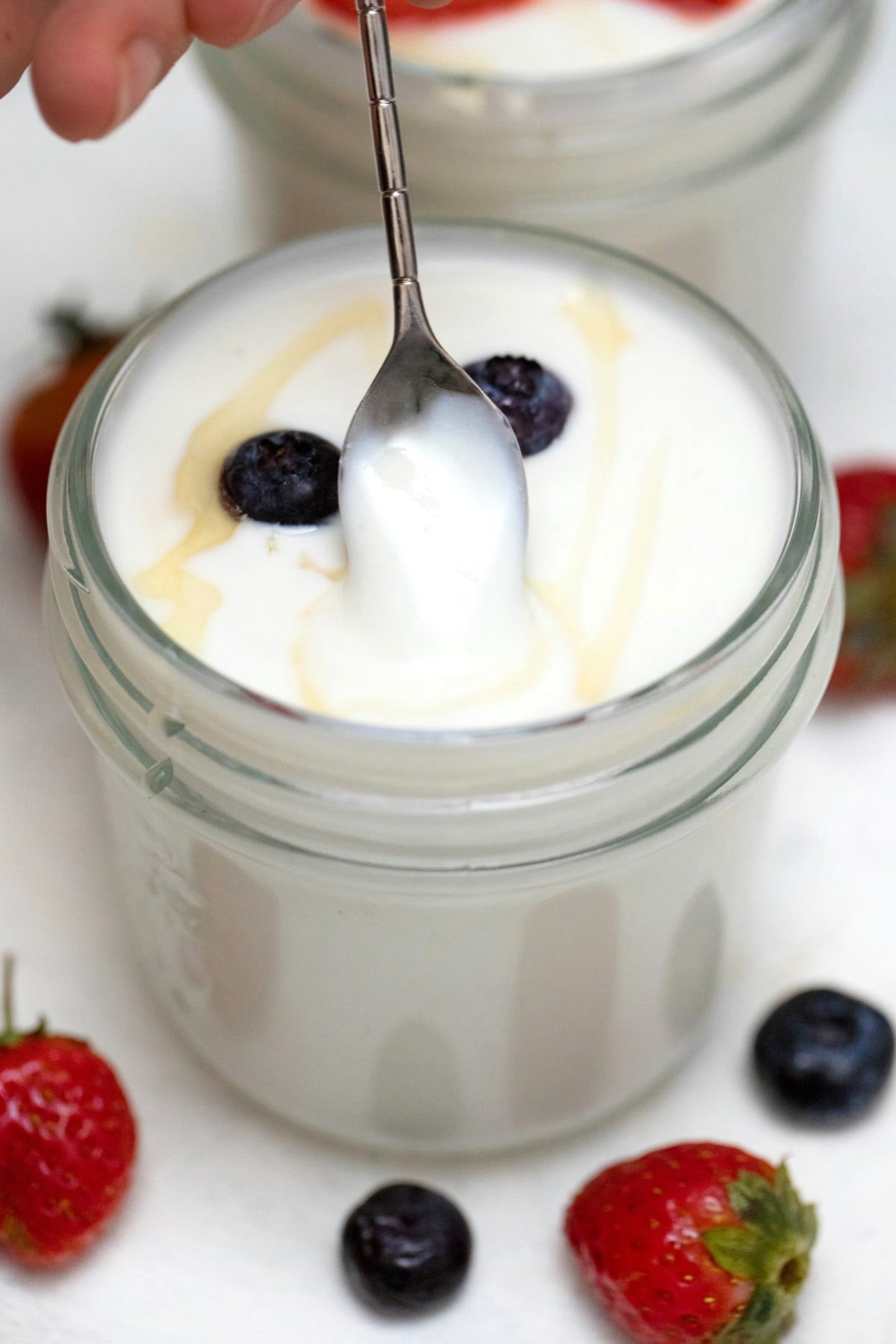 Yogurt in glass jar with honey and blueberries on top.