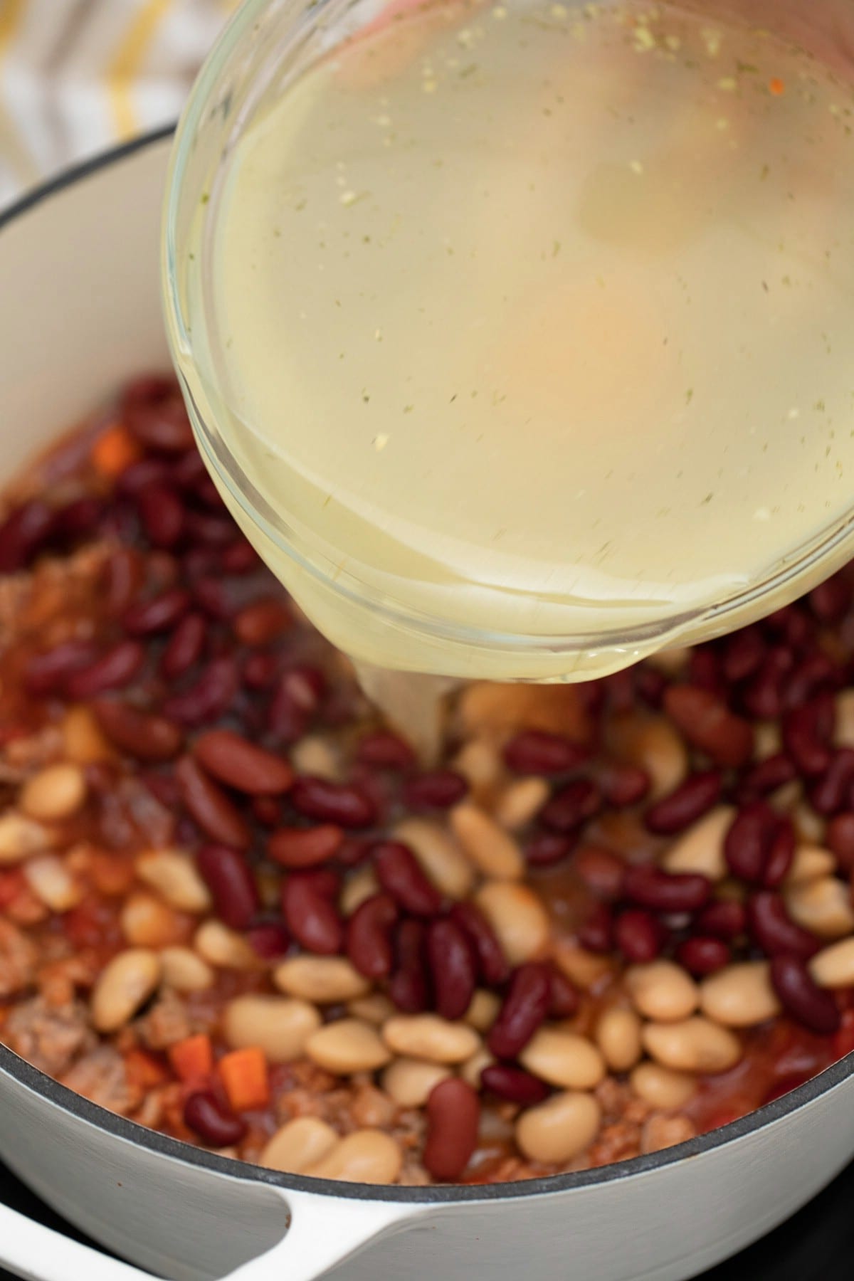 Adding broth to pan with beans and meat