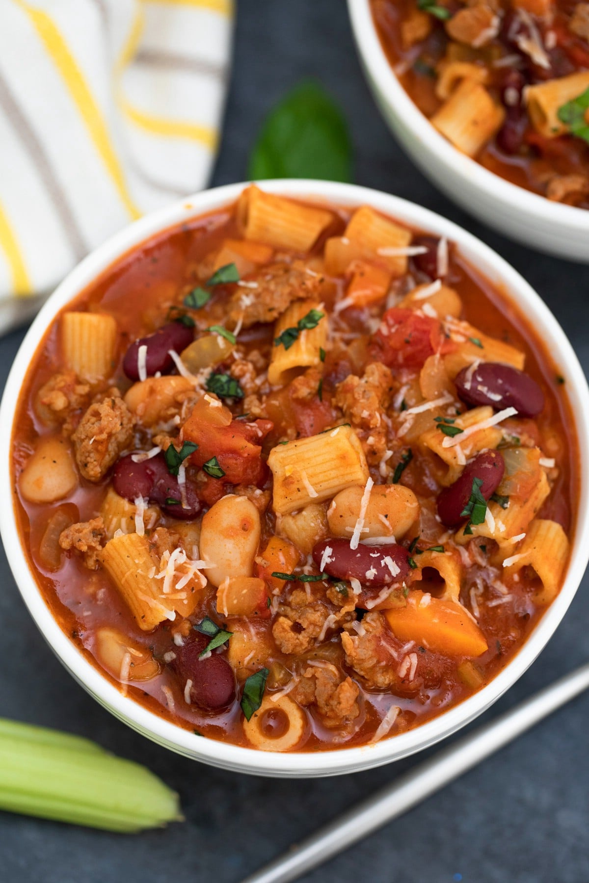 Large white bowl of soup on dark table with striped napkin in background