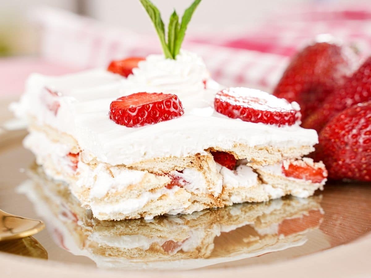 Side view of icebox cake on tan plate topped with strawberry slices and mint