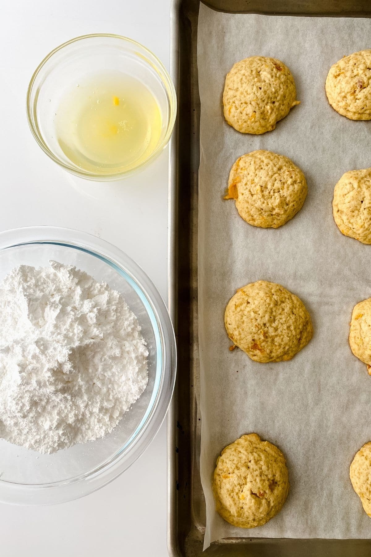 Baked cookies on baking sheet with bowl of powdered sugar on side