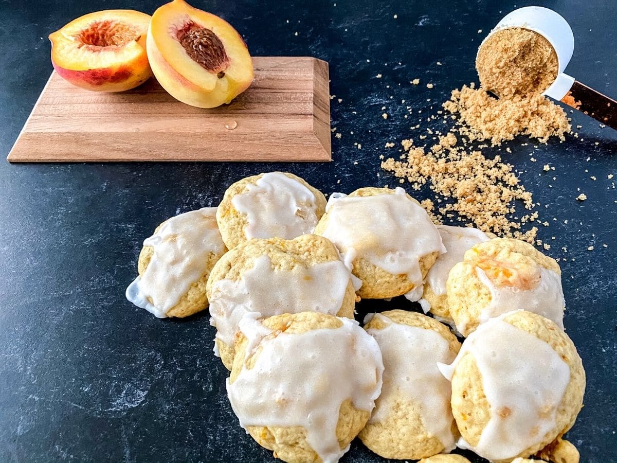 Cookies with glaze on counter next to cutting board with peach