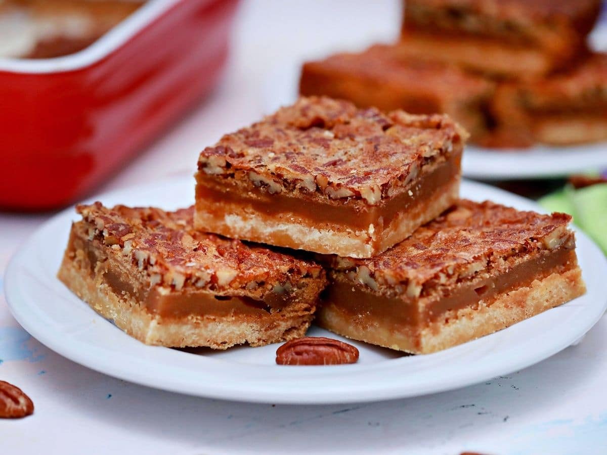Three pecan pie bars on white saucer by red baking dish