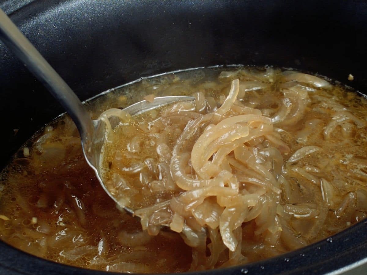 Metal spoon of soup above black slow cooker