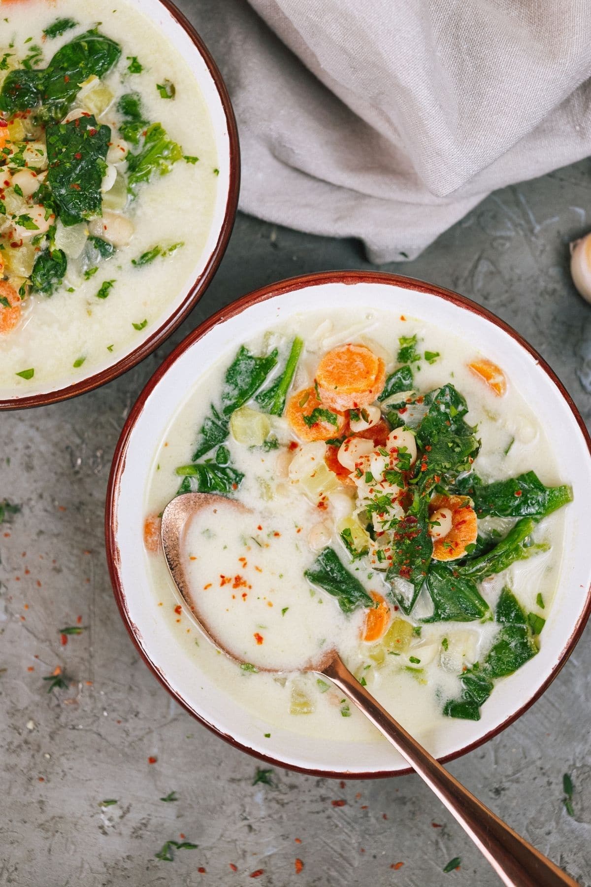 Two white bowls of soup with spinach on gray counter