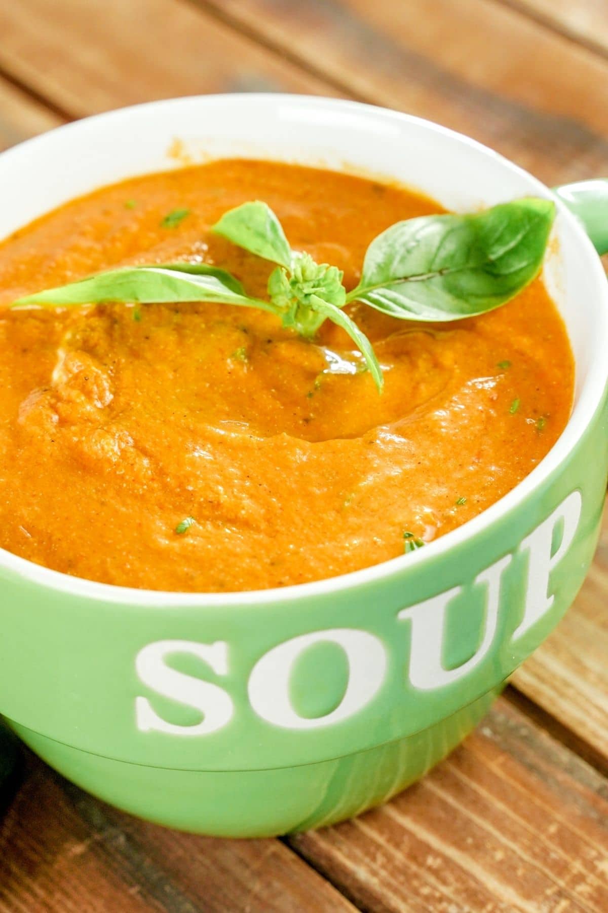 green mug with soup written in white filled with soup topped with basil
