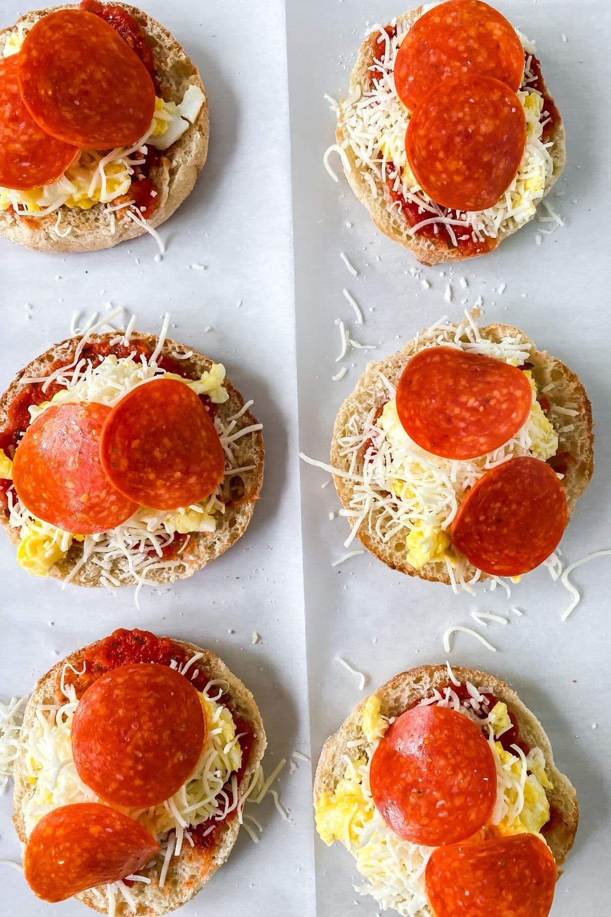 pepperoni on top of english muffin pizza on baking sheet