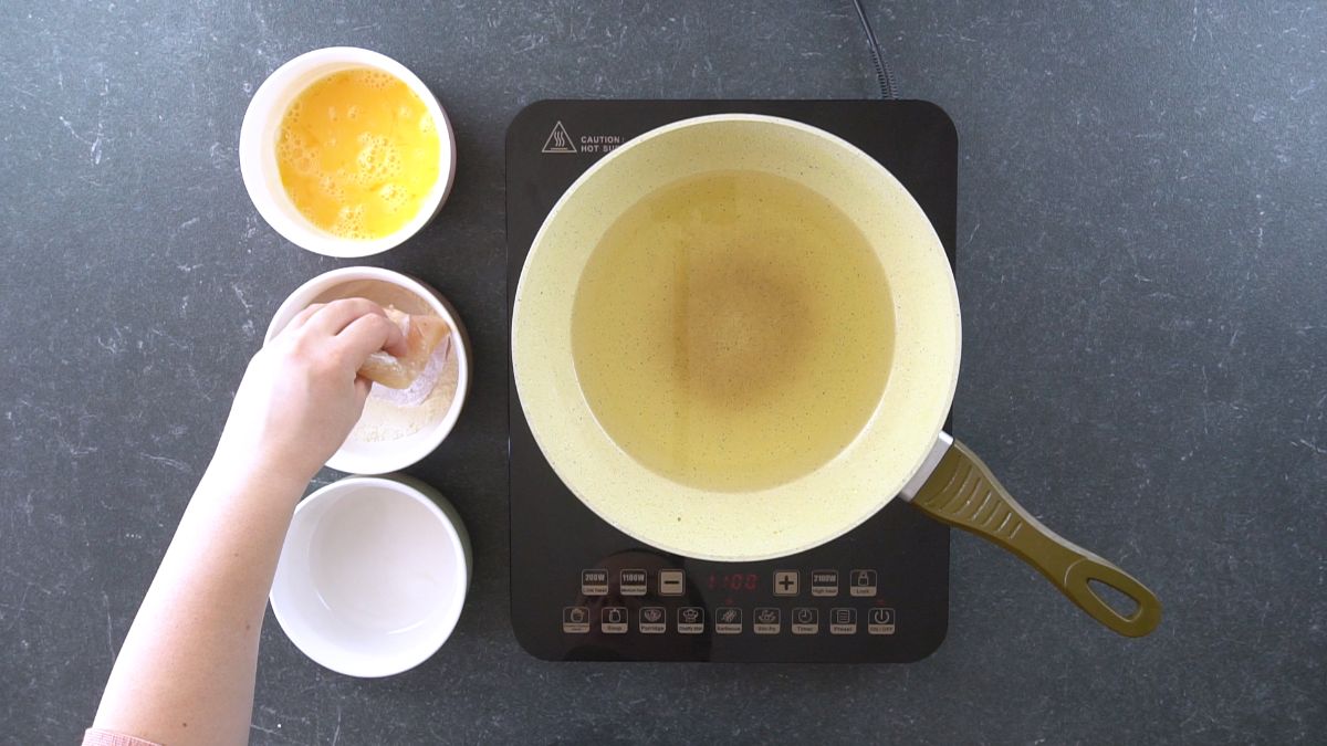 hand dredging chicken by hot plate holding skillet
