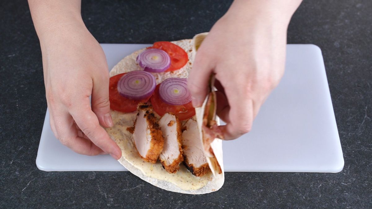 hand folding tortilla wrap on cutting board