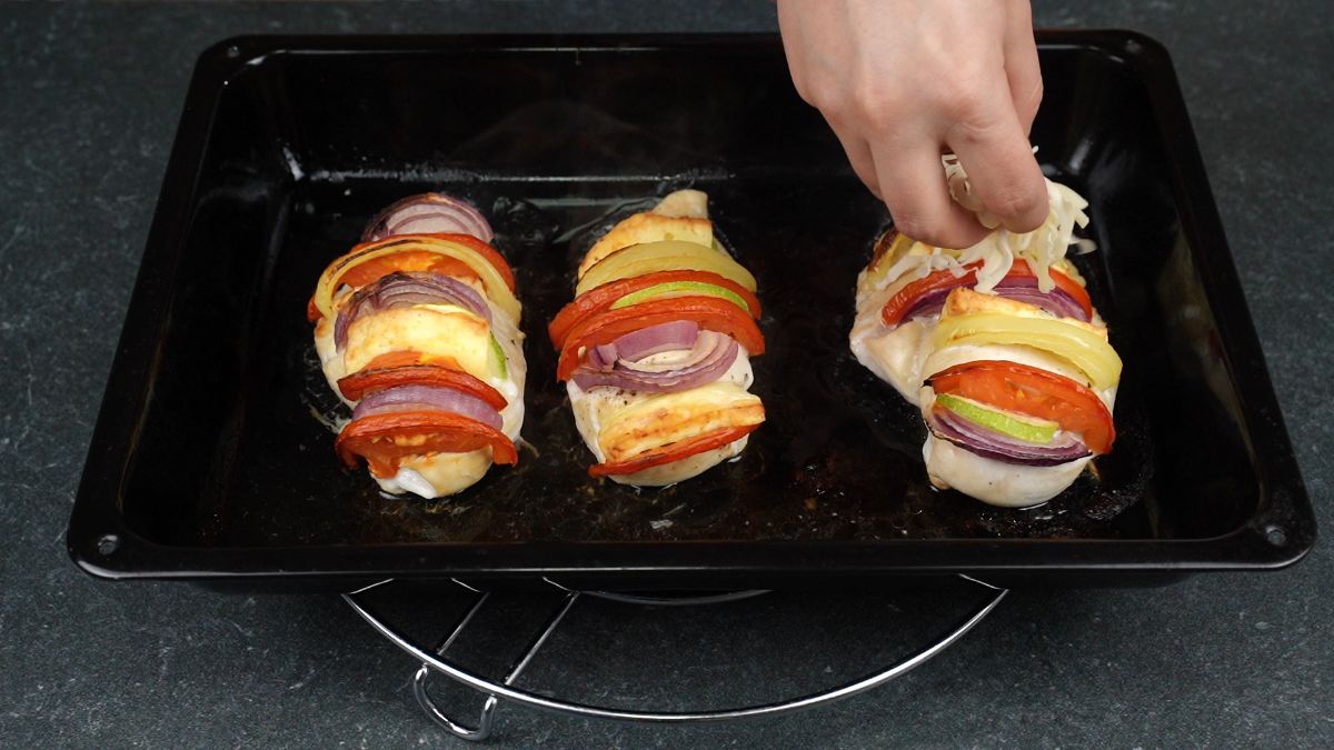 hand sprinkling cheese on top of chicken breasts in black baking dish