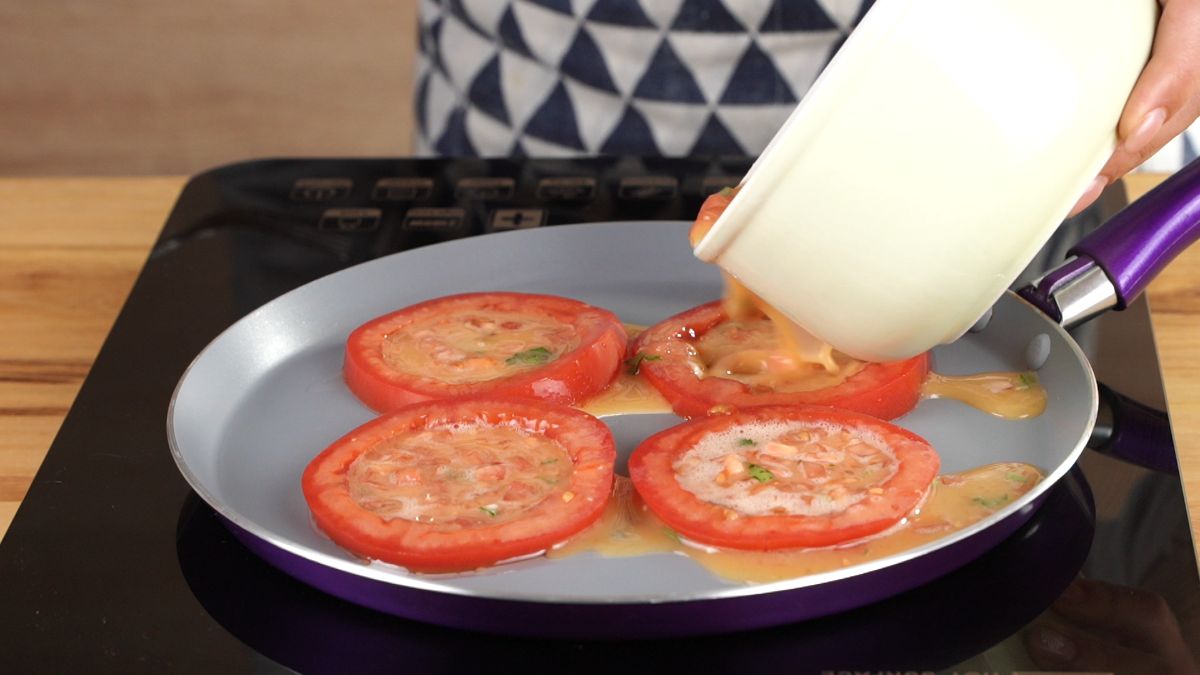 tomato rings with egg in them in skillet on black hot plate sitting on wooden table