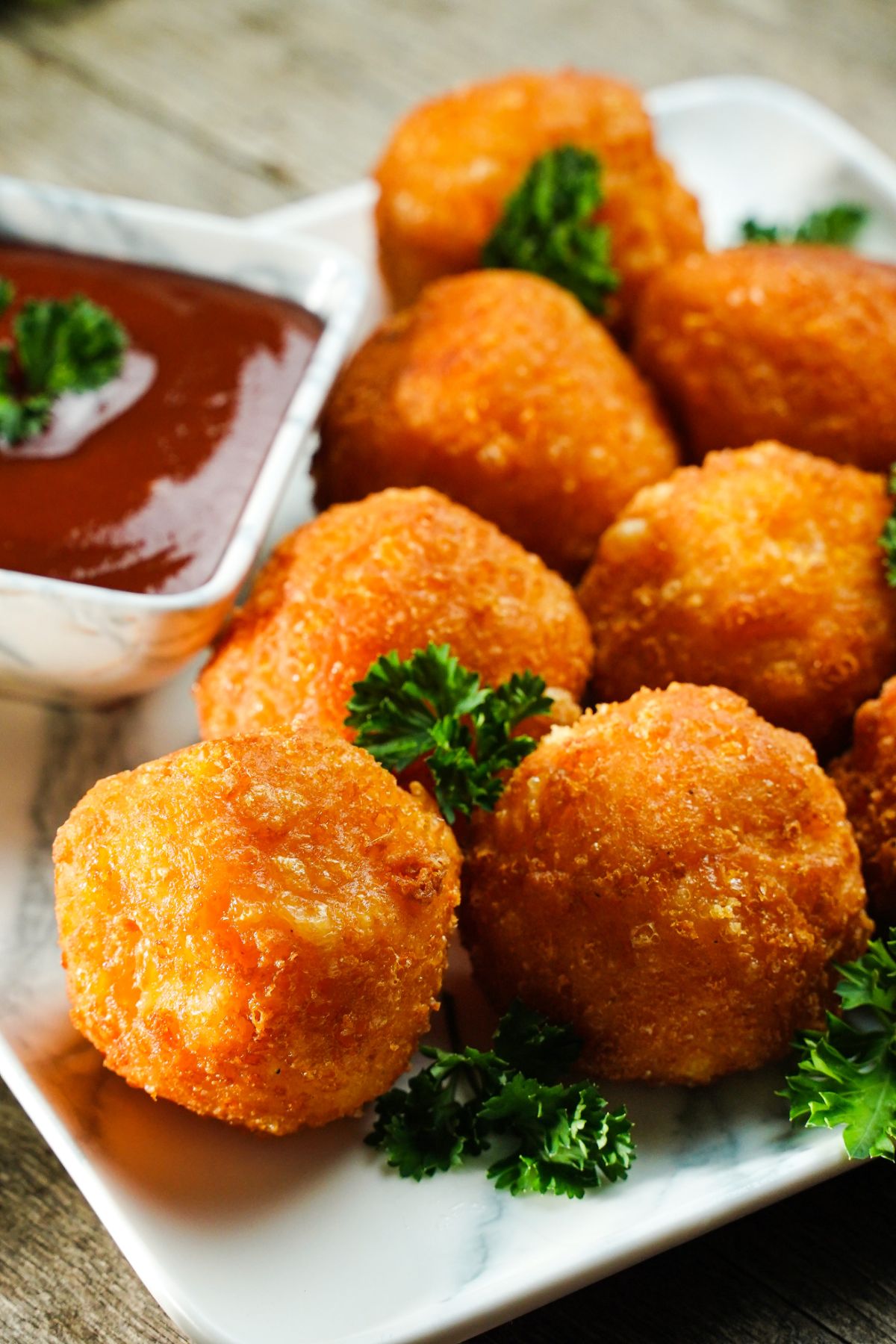 stacks of cheese balls on marble plate with parsley on top and small bowl of red sauce on the side