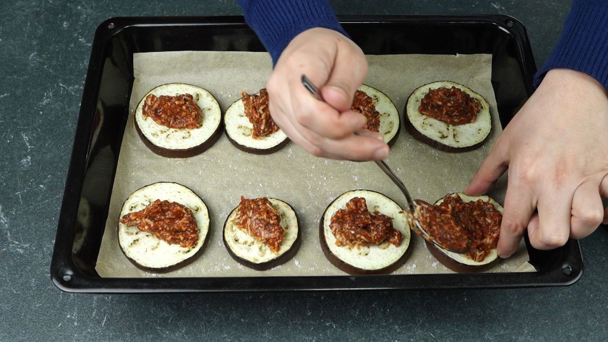 hand spooning sauce onto eggplant rounds