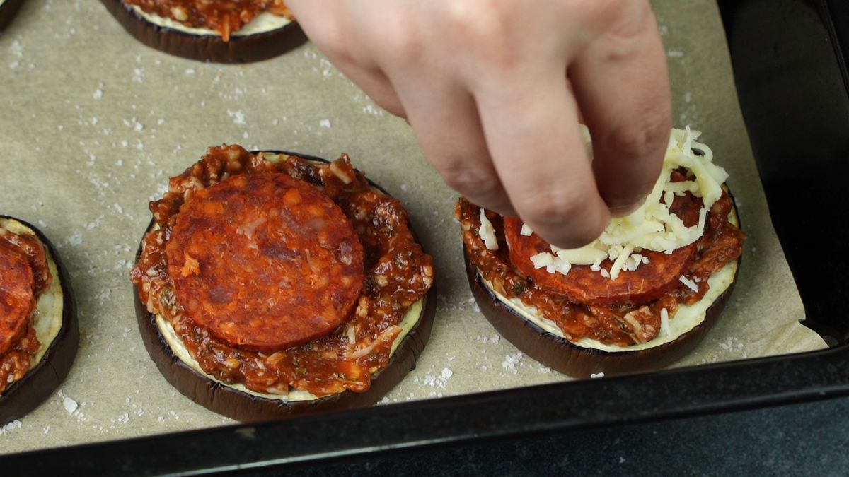 hand sprinkling cheese on top of eggplant pizza