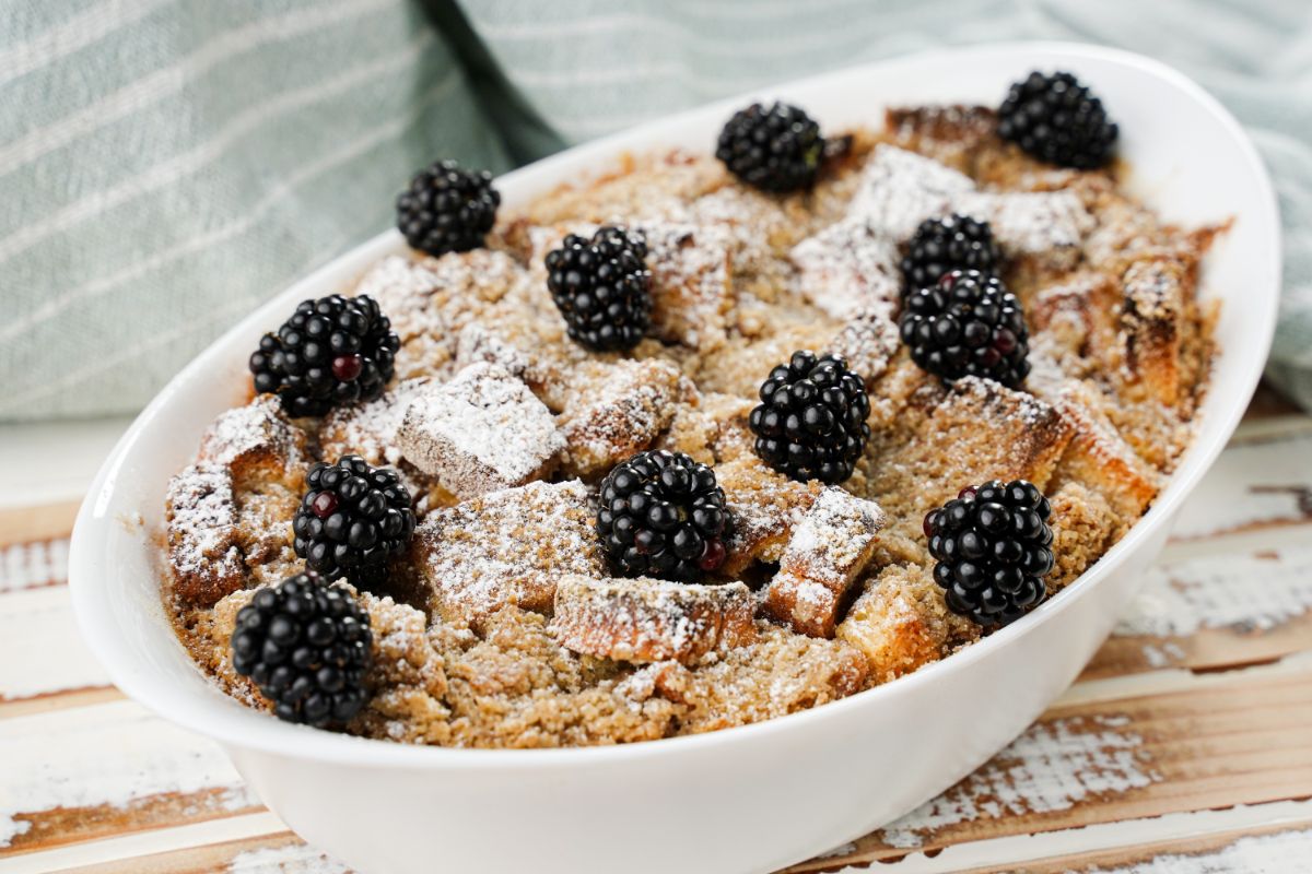 oval white baking dish of french toast topped with powdered sugar and blackberries