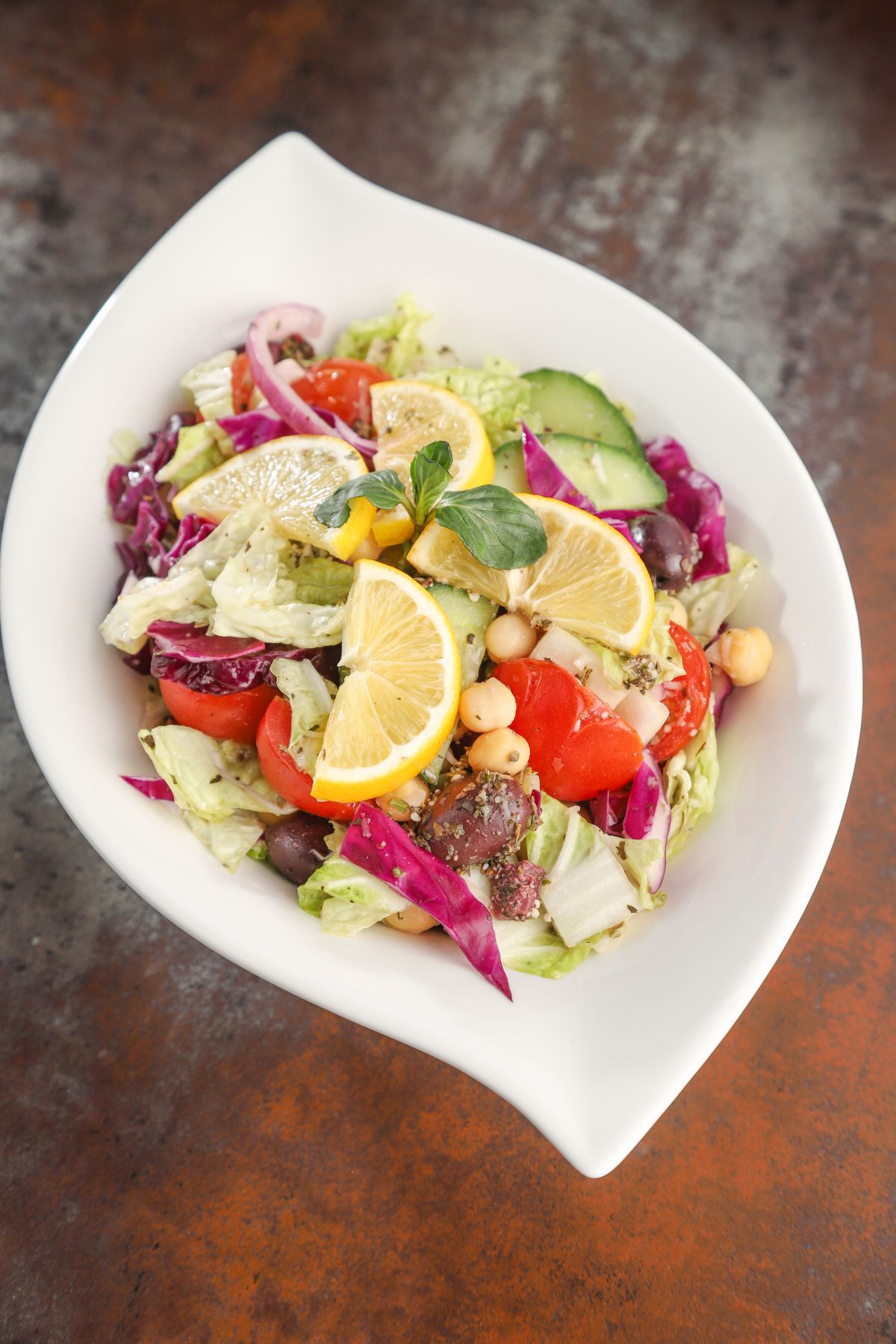 lemon wedges on top of salad in white oval bowl on wood table