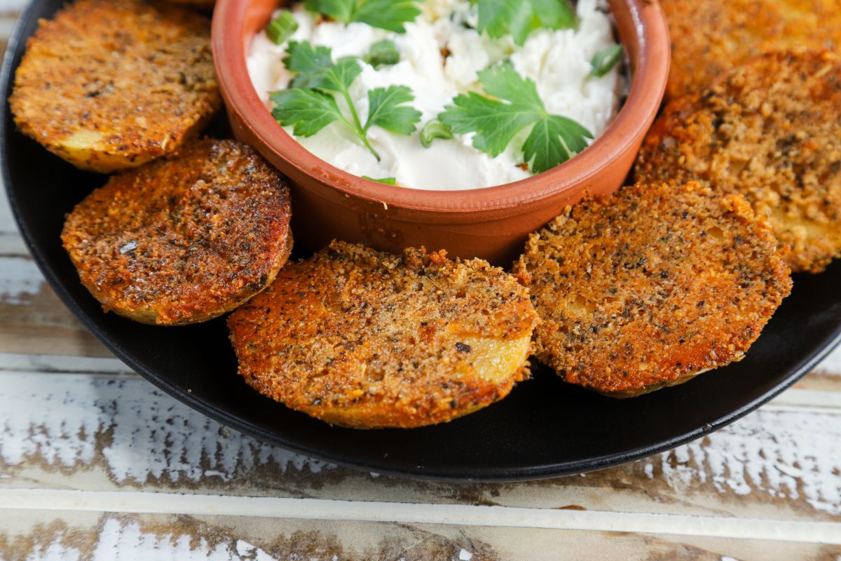orange bowl of white dip in center of black plate with roasted potatoes