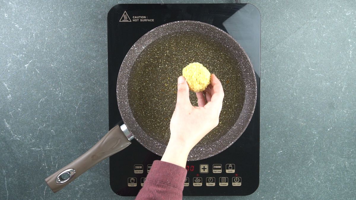 hand holding chicken ball above skillet of hot oil