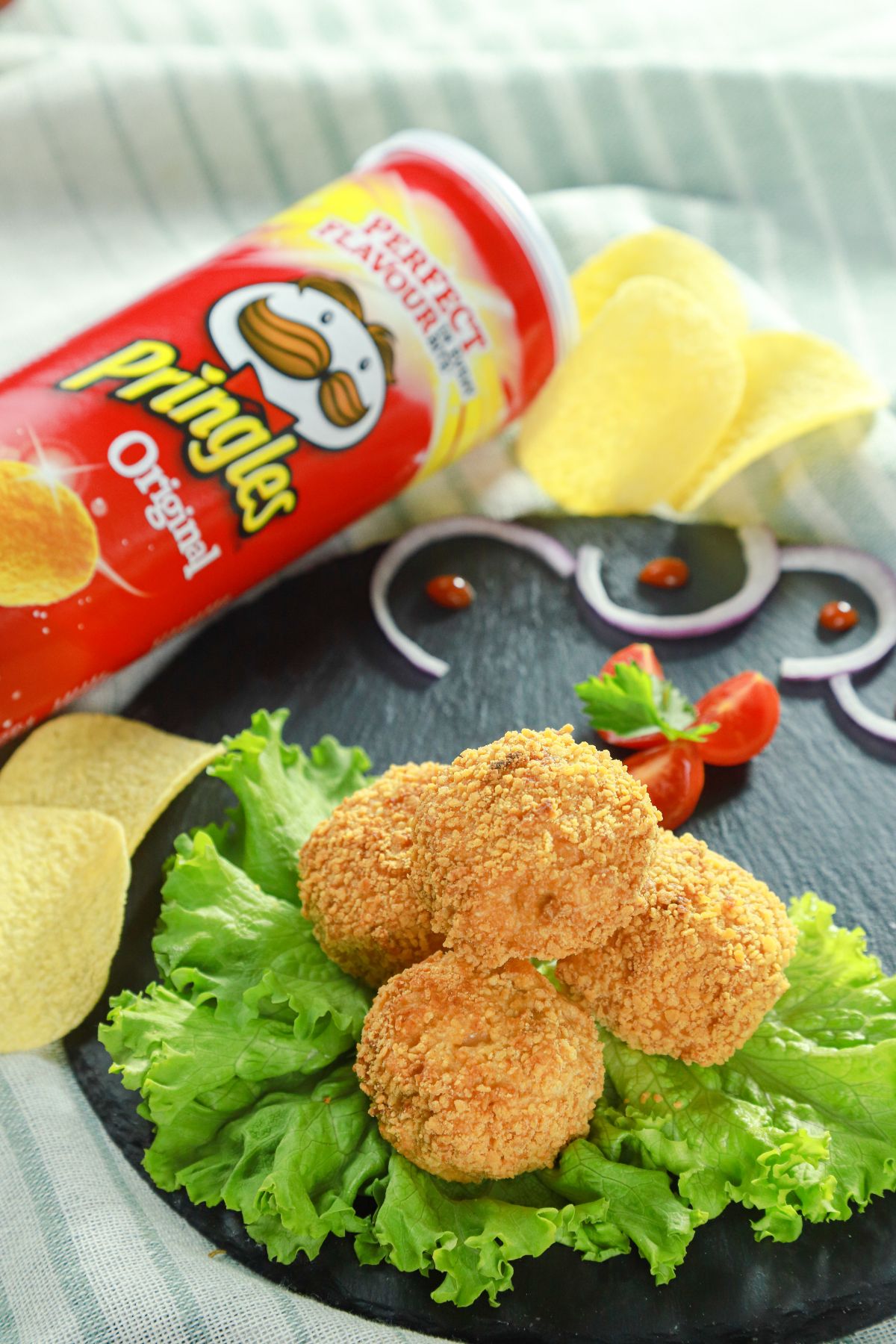 pringles can laying on table behind black plate of chicken bombs