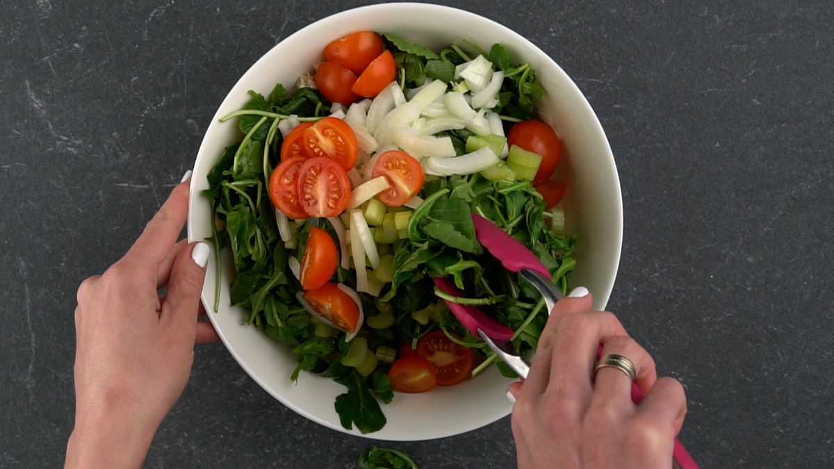 salad being tossed with pink tongs