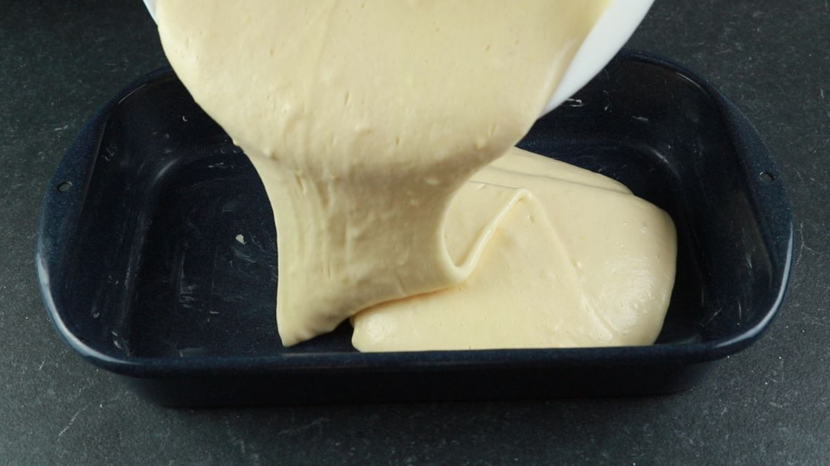 white bowl of batter being poured into cake pan