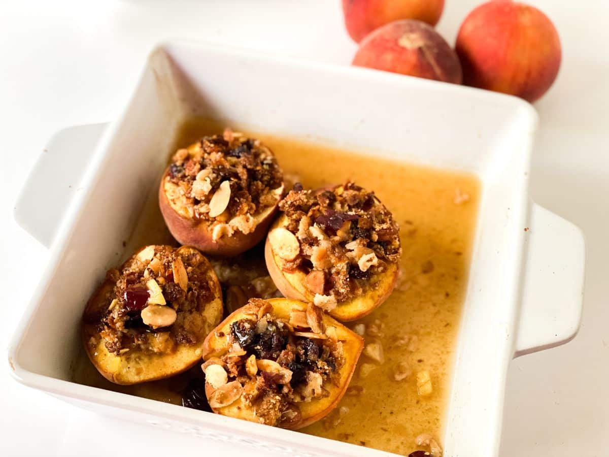 square baking dish of baked peaches on table by raw peaches